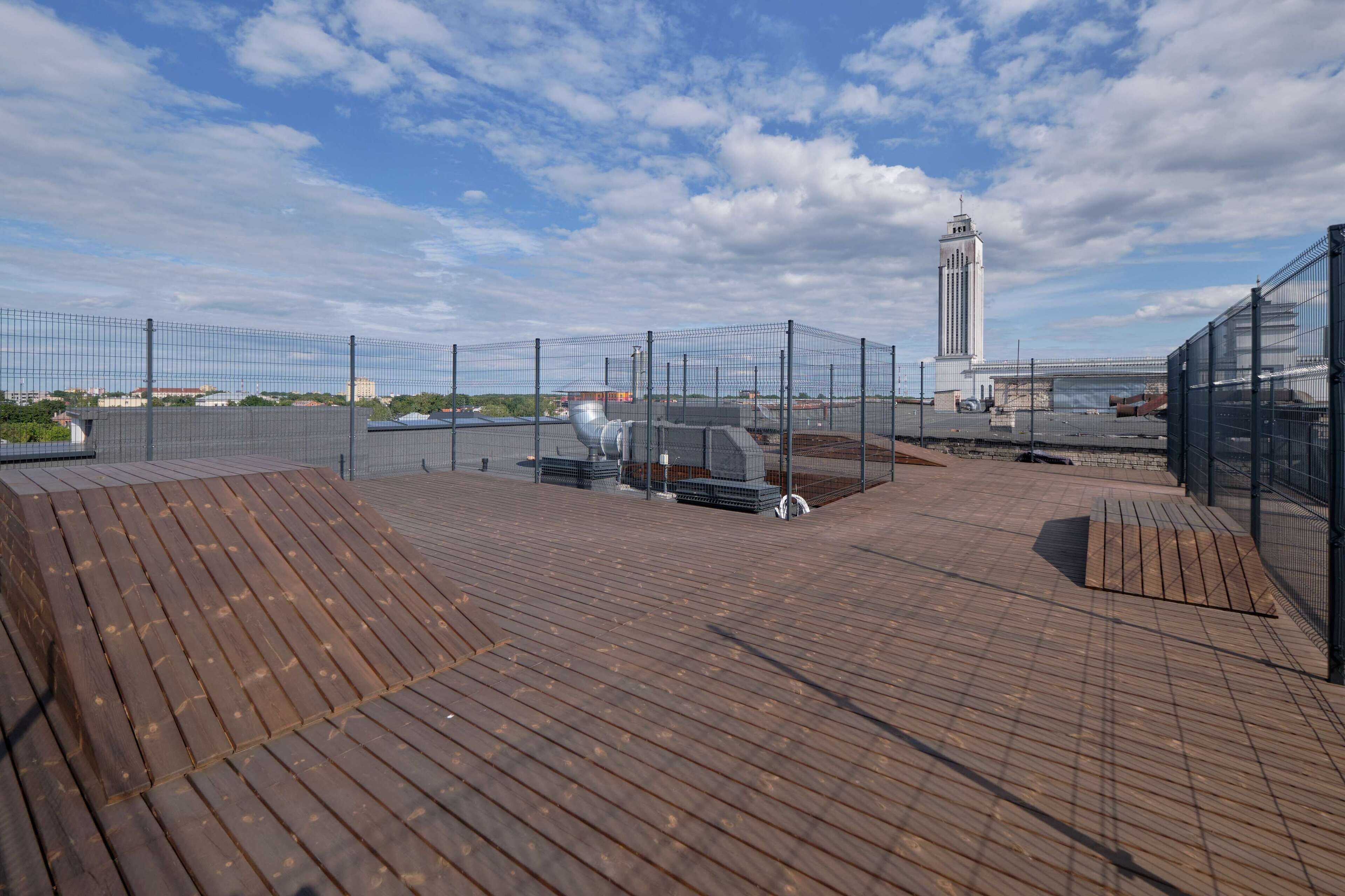 Une terrasse sur le toit offrant une vue sur une haute tour, entourée de clôtures et surplombant un ciel dégagé.