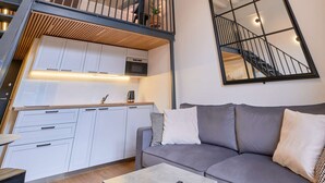 A modern loft apartment with a kitchen, a gray sofa, and a staircase with a railing. - Queen Barbora Central Lofts (Kaunas)
