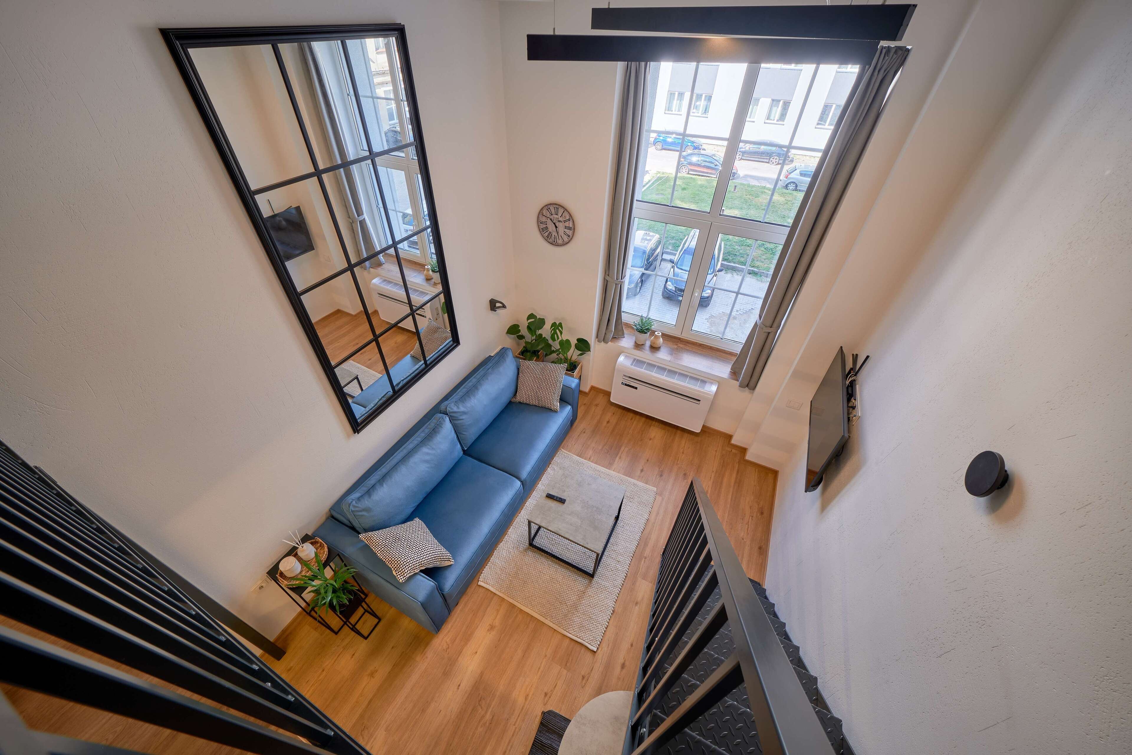 A modern living room with a blue sofa, a large window, and a staircase.