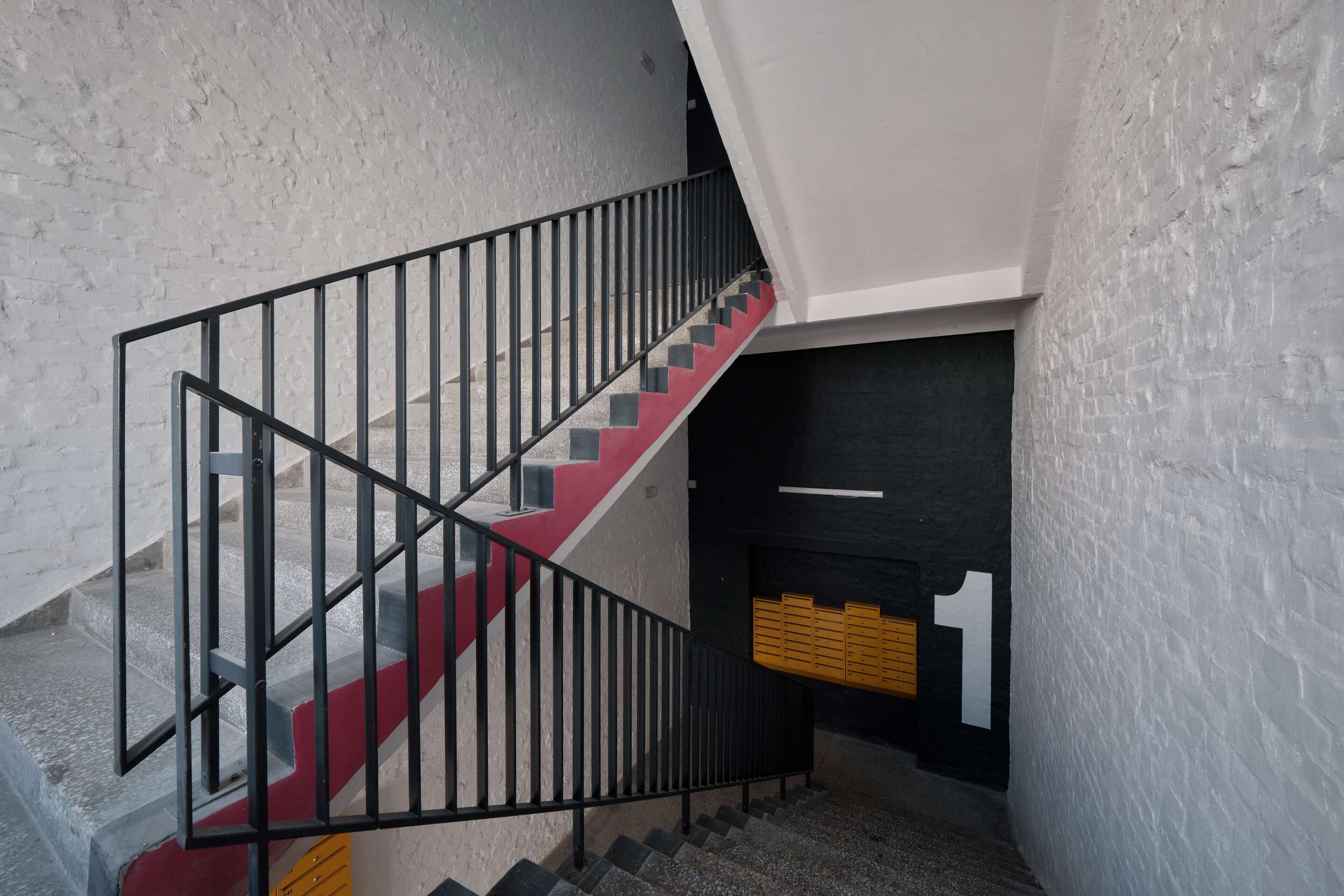 Una escalera con barandillas negras y peldaños rojos, que conduce a una puerta con un cartel grande con el número 1.