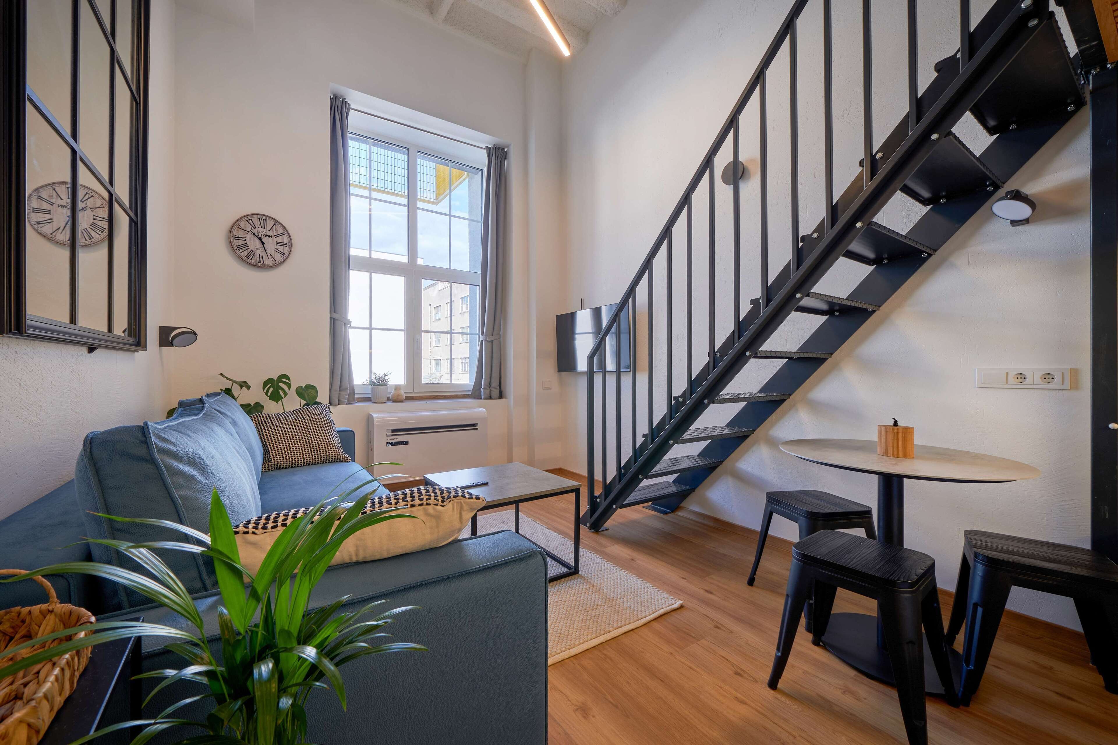 Een moderne woonkamer met een trap, een bank, een salontafel en een bijzettafeltje met een kaars.