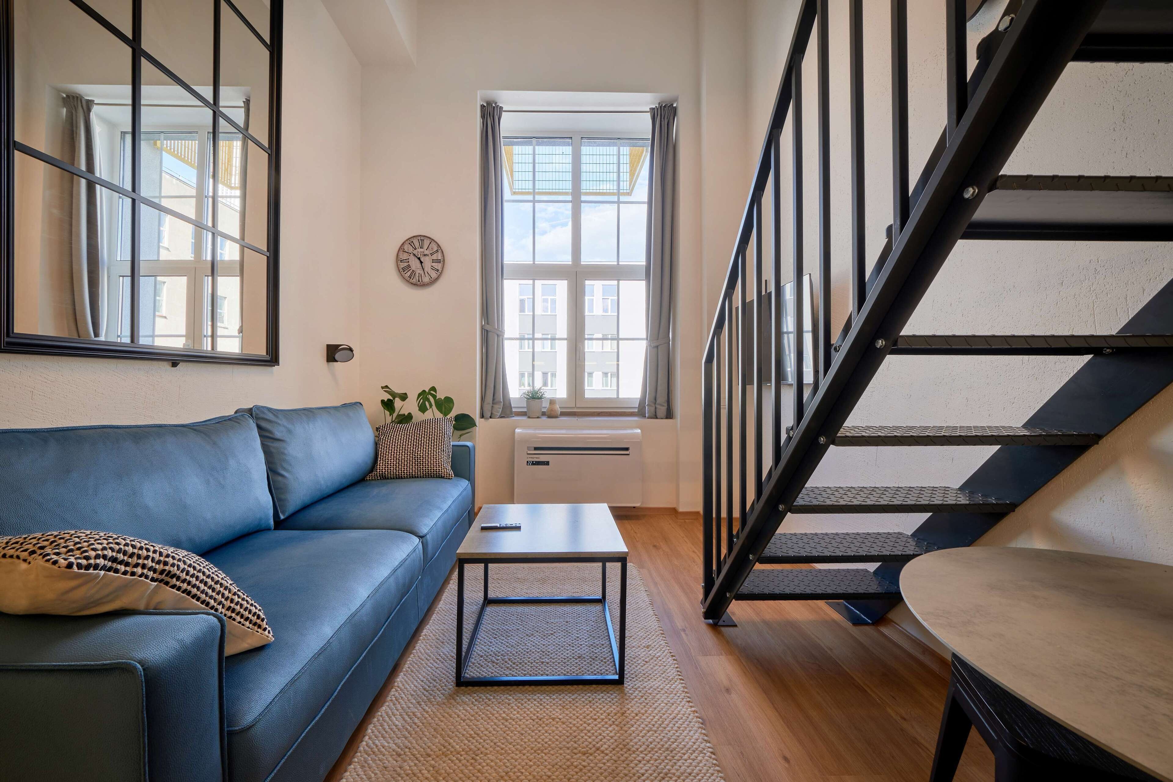 A modern living room with a blue sofa, a coffee table, and a staircase.