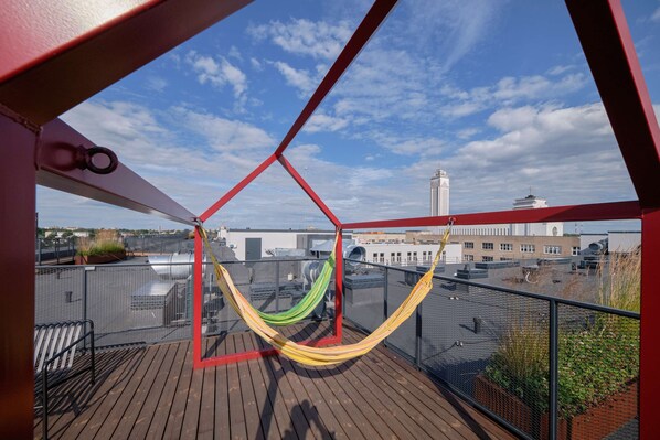 Un hamac sur une terrasse en bois, avec vue sur les bâtiments et un ciel dégagé.