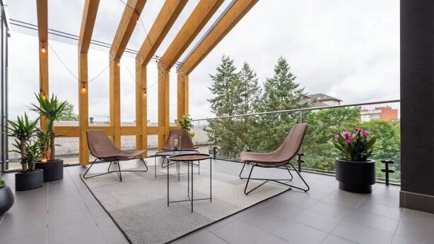 A modern outdoor seating area with two chairs and a table, surrounded by potted plants and a view of trees and buildings. - Luxurious penthouse with parking
 (Riga)
