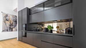 A modern kitchen with dark cabinetry, a countertop, and a large window above the sink. - Luxurious penthouse with parking
 (Riga)