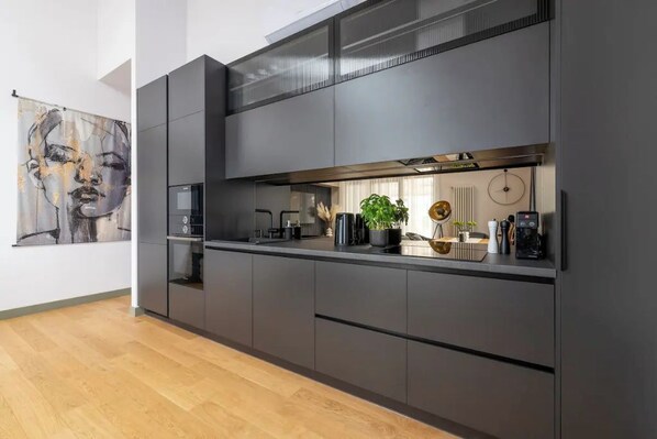 A modern kitchen with dark cabinetry, a countertop, and a large window above the sink.