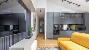 A modern kitchen with grey cabinets, a black countertop, and a yellow sofa in a bright living area. - Luxurious penthouse with parking
 (Riga)
