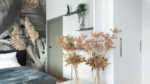 A bedroom with a bed, a white bedside table with vases, a wall with a large shark skeleton mural, and a door with a plant shelf. - Luxurious penthouse with parking
 (Riga)