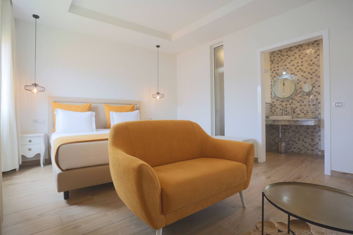 Un dormitorio moderno con cama, sofá, mesa de comedor y baño visible a través de una puerta abierta.