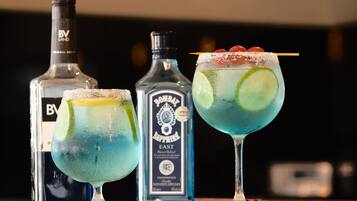 Drie cocktails met garnering, een fles Bombay Sapphire gin en een fles B.V. Land wodka.