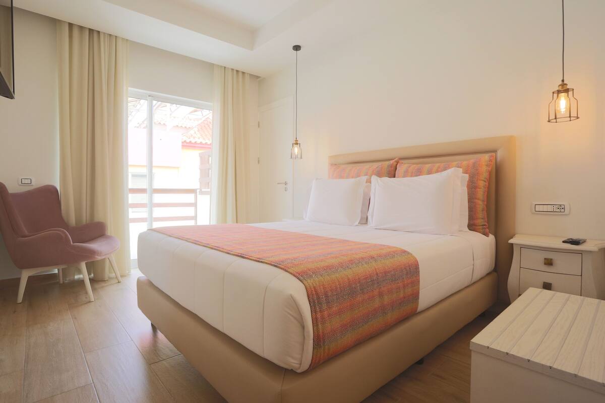 Una habitación de hotel con una cama grande, una silla, una mesita de noche y un ventanal con cortinas.