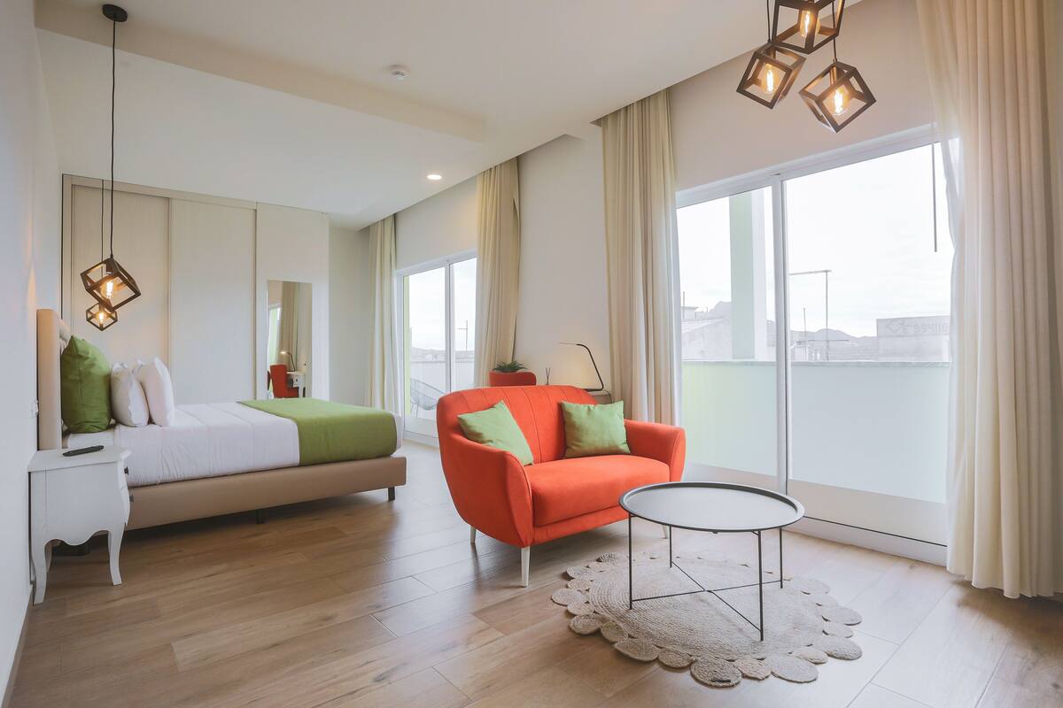 Una habitación de hotel moderna con una cama, un sofá, una mesita y ventanas amplias.