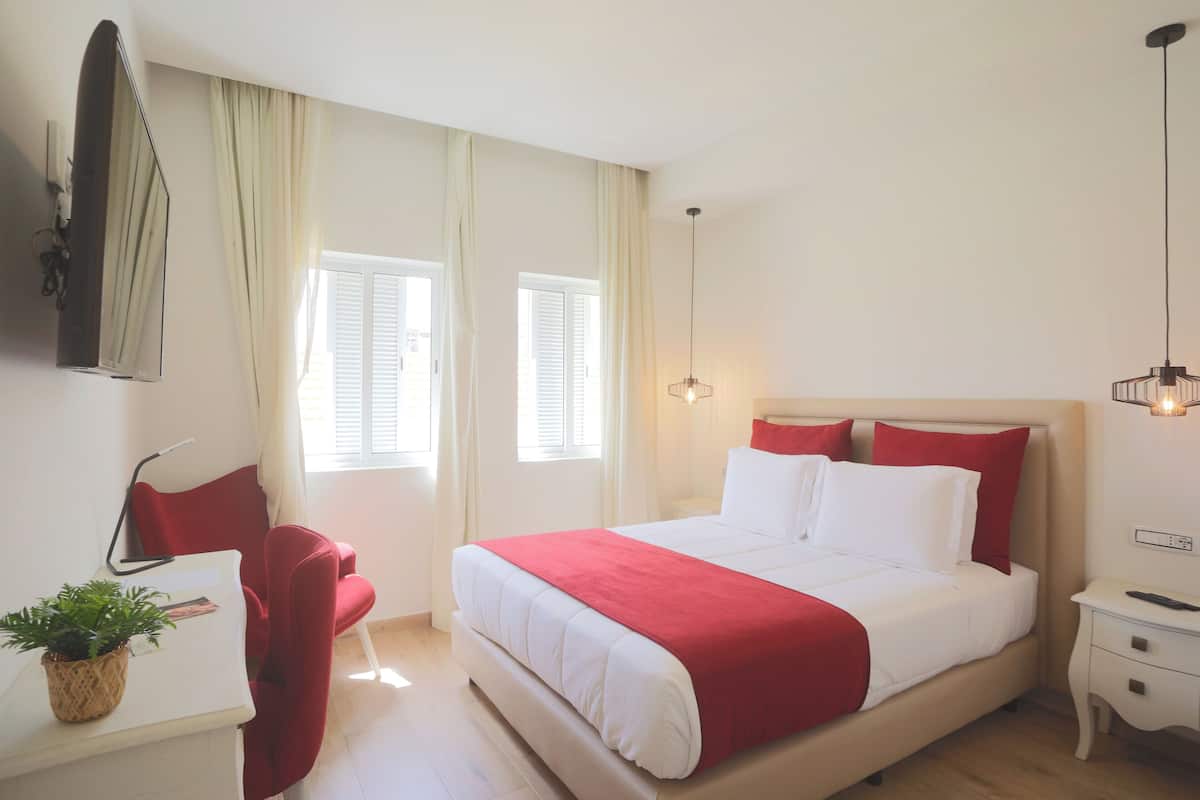 Habitación de hotel ordenada con cama, mesita de noche, lámpara y una planta en maceta.