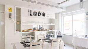 Un comedor moderno con una mesa blanca dispuesta para cuatro personas, un mostrador de buffet con comida y bebidas, y un letrero sobre el mostrador que dice 