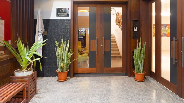 Entrada de un hotel con puerta de madera, plantas en macetas, un banco y una escalera que conduce al interior.
