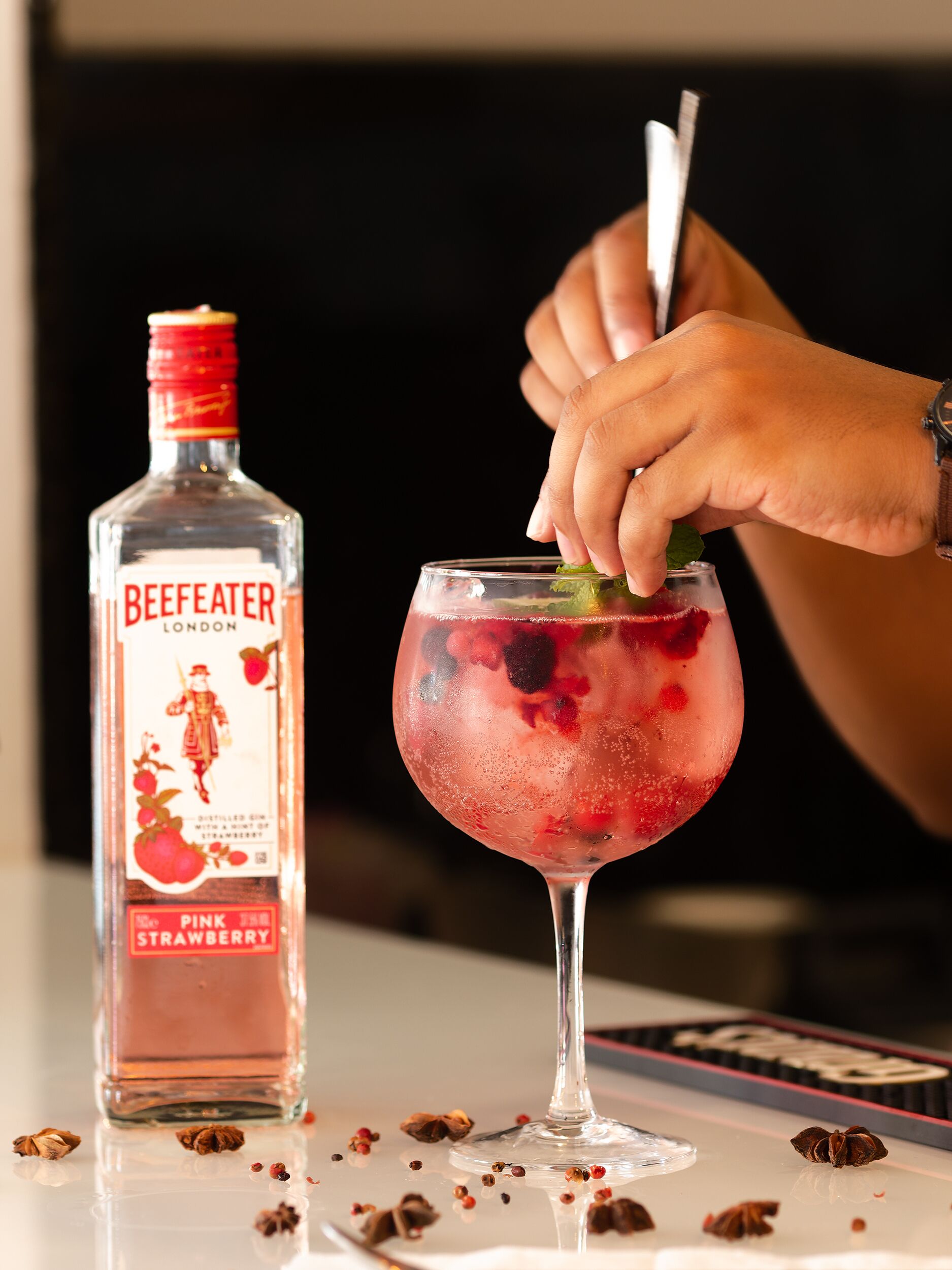 Una botella de vodka BeefEater London Strawberry y una copa con hielo y bayas.