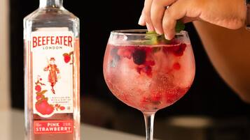 Una botella de vodka BeefEater London Strawberry y una copa con hielo y bayas.