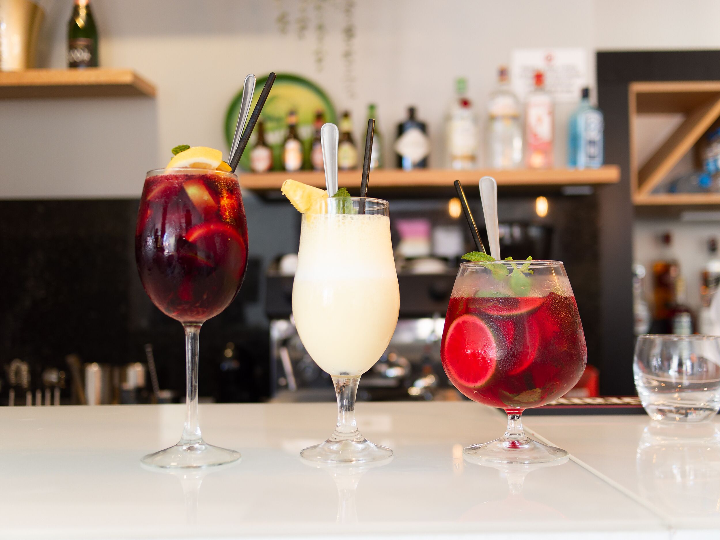 Three drinks on a bar counter with a blurred background of shelves and bottles.