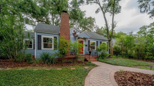 A two-story house with a brick chimney, a front porch, and a pathway leading to the entrance.