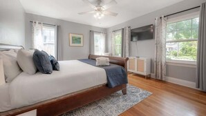 A bedroom with a bed, a ceiling fan, a TV mounted on the wall, and a window with curtains.