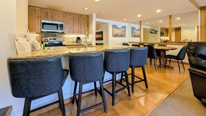 A modern kitchen with a central island, bar stools, and a dining area with a large table and chairs. - Keystone Lake Stay | King Beds + Summer Fun (Keystone)