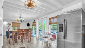A modern kitchen with a stainless steel refrigerator, wooden dining table, and chairs. - Tipsy Turtle: Warm and Inviting, Short Walk to the Beach (Oak Island)