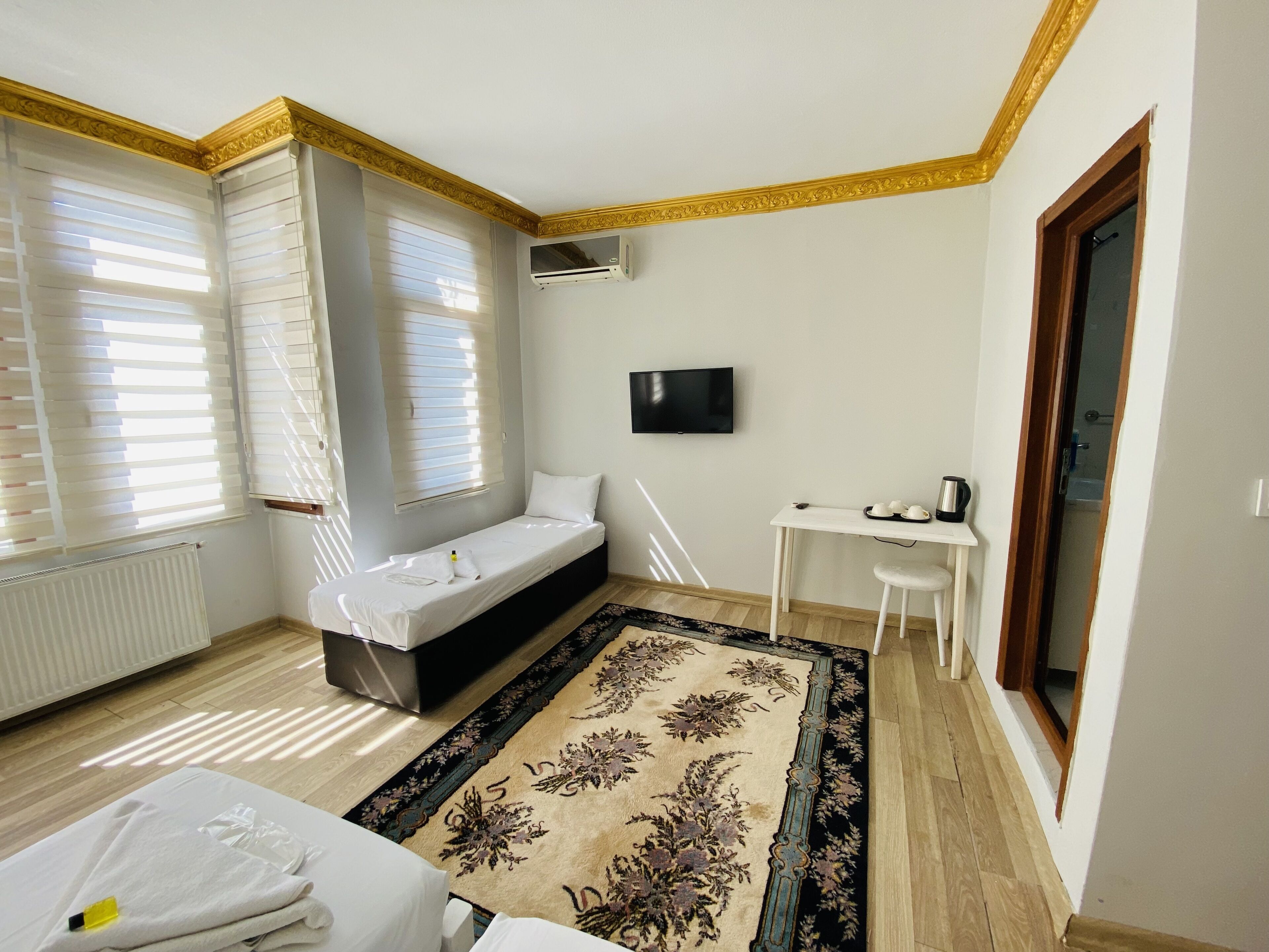 A hotel room with a bed, a small desk with a chair, a television, and a window with blinds.