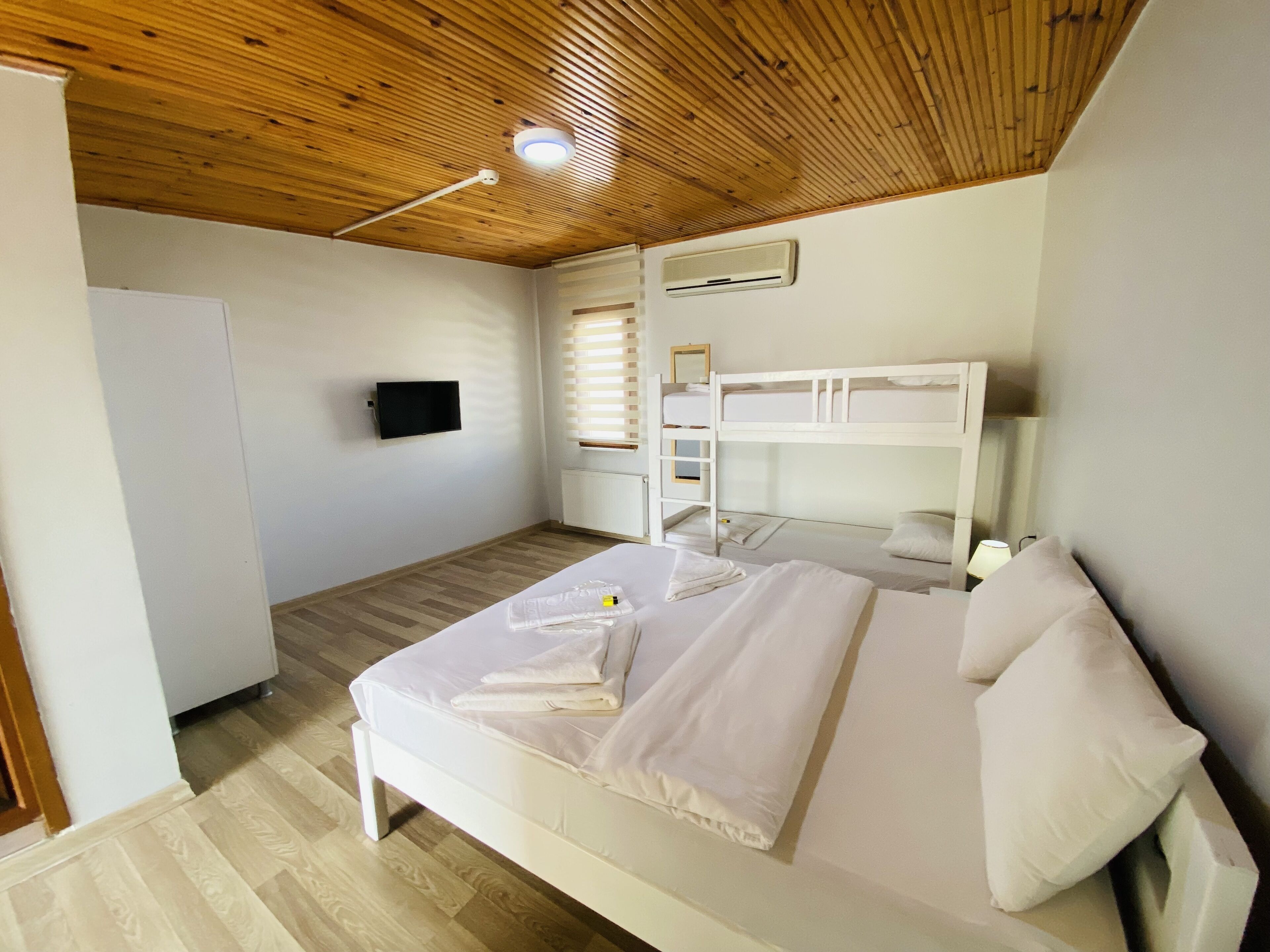 A bedroom with a bunk bed, a flat-screen TV, a heater, and a window with blinds.