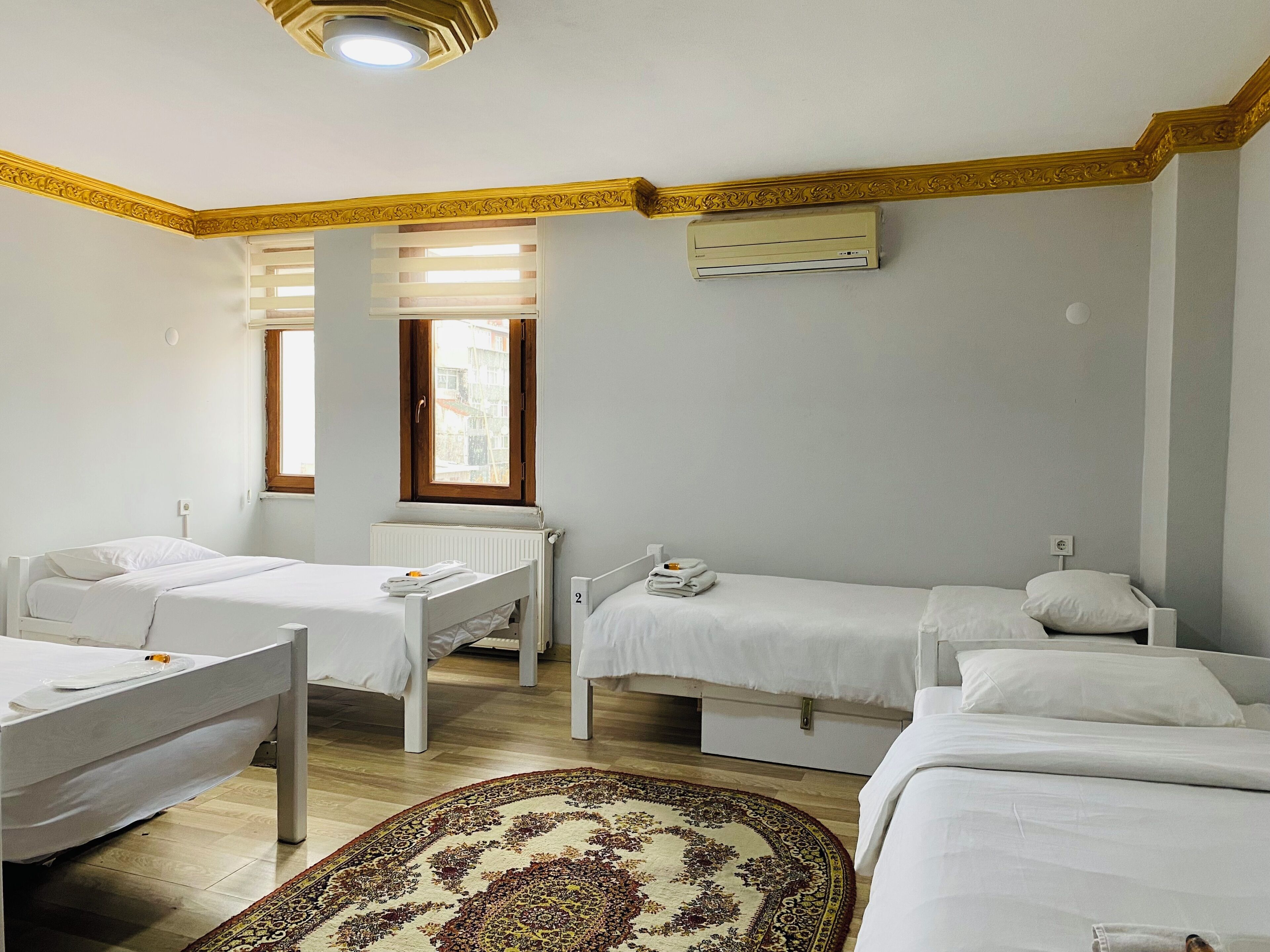 A hotel room with two single beds, a small desk, a radiator, and a window with blinds.