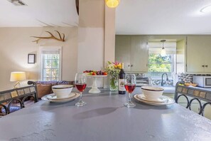 Een eethoek met een lange tafel gedekt voor twee personen, een bloevas en een fles wijn.