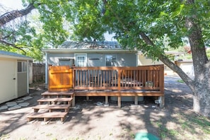 A wooden deck with steps leading to a covered seating area, a small shed, and a tree in the background.