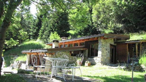 A rustic stone house with a wooden deck, surrounded by lush greenery. - Chalet de Bébert (Conthey)