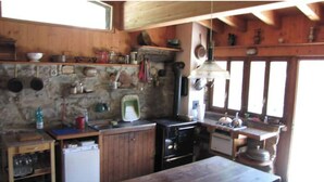 A rustic kitchen with wooden walls, a stone backsplash, and basic appliances. - Chalet de Bébert (Conthey)