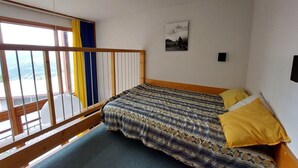 Un dormitorio con cama, ventana con cortinas, un cuadro en la pared y un balcón con barandilla.