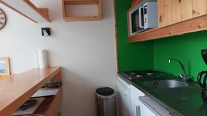 Cocina pequeña con salpicadero verde, armarios de madera, un lavamanos de acero inoxidable y un lavavajillas compacto.