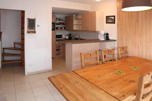 Cocina compacta con armarios de madera, microondas y cafetera. Hay una mesa de comedor con sillas y una pequeña isla con fregadero.