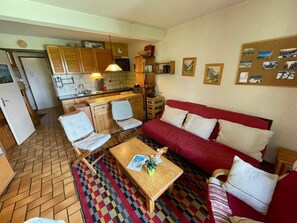 Ein kleiner Wohnbereich mit Küchenzeile, einer Couch, einem Couchtisch und einem gemusterten Teppich.