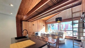 Una cocina moderna con una isla central, vigas de madera en el techo y un comedor con sofá y sillas.