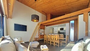 Una sala de estar acogedora con techo de madera, un comedor con sillas de madera y una cocina al fondo.