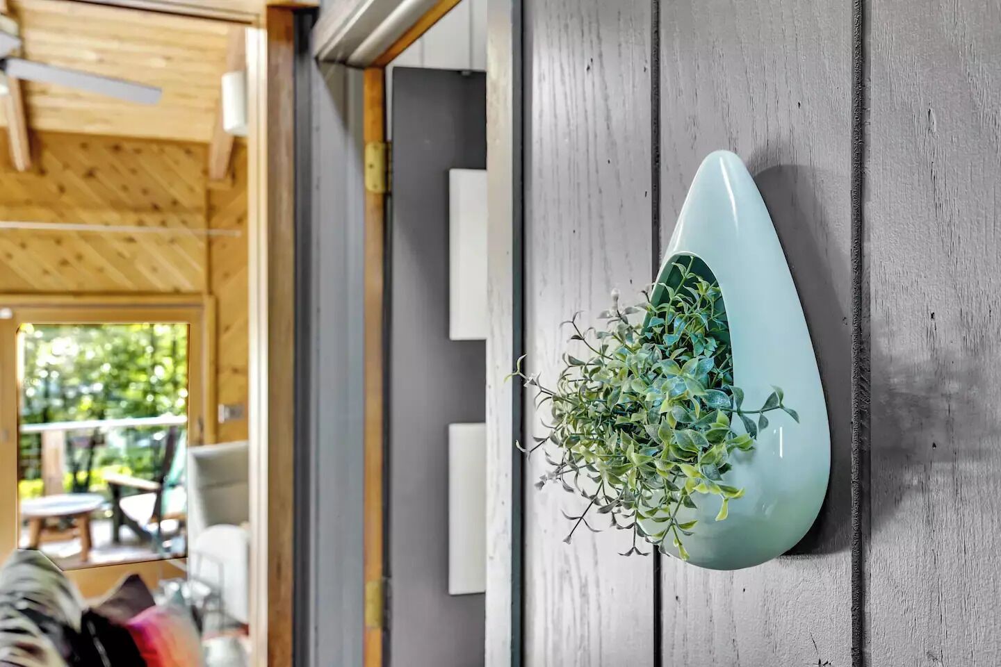 Un intérieur moderne avec un plafond en bois, un jardinier mural gris orné de plantes vertes, et un aperçu d’un espace extérieur aménagé pour se détendre.