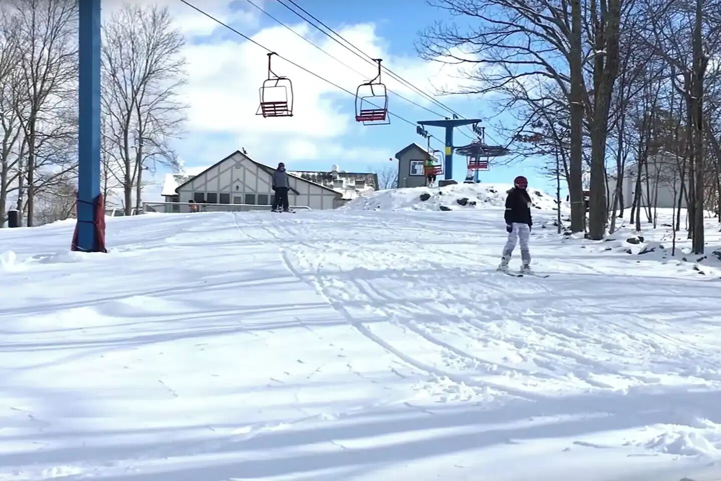 A ski slope with a chairlift, trees, and a building in the background.