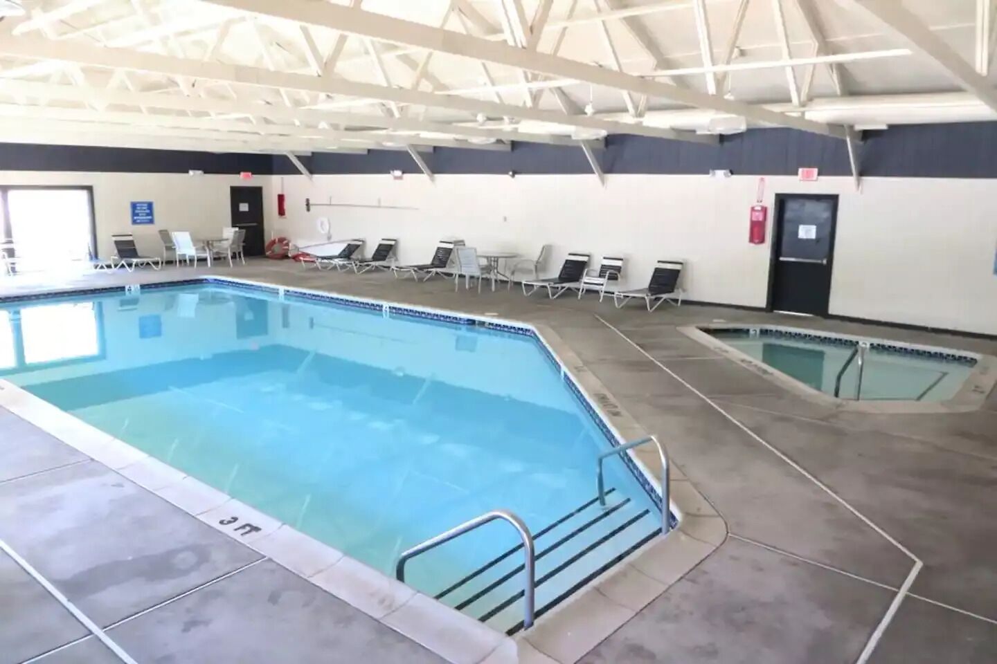 An indoor swimming pool with multiple lanes, lounge chairs, and a ceiling with structural beams.