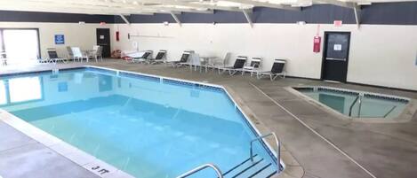An indoor swimming pool with multiple lanes, lounge chairs, and a ceiling with structural beams.