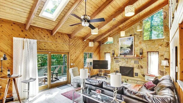 A spacious living room with a stone fireplace, leather sofa, and a large TV.