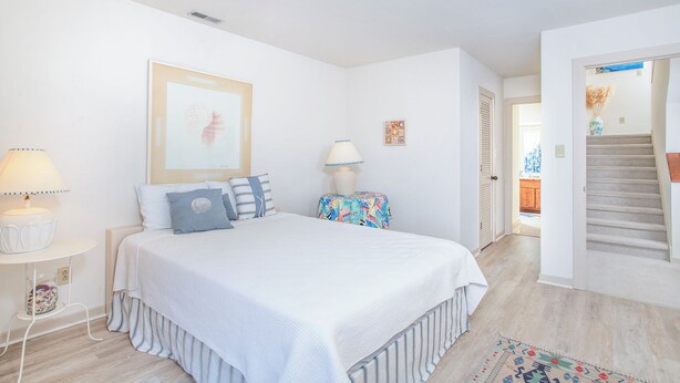 A bedroom with a bed, bedside tables, a lamp, a framed artwork, and a staircase leading to another room. - 4 BDR/Ocean Front Ocean Grove J2 Condo (Salter Path)