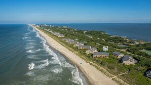 An aerial view of a coastal residential area with beachfront properties, including multi-story buildings and a beach access path.
