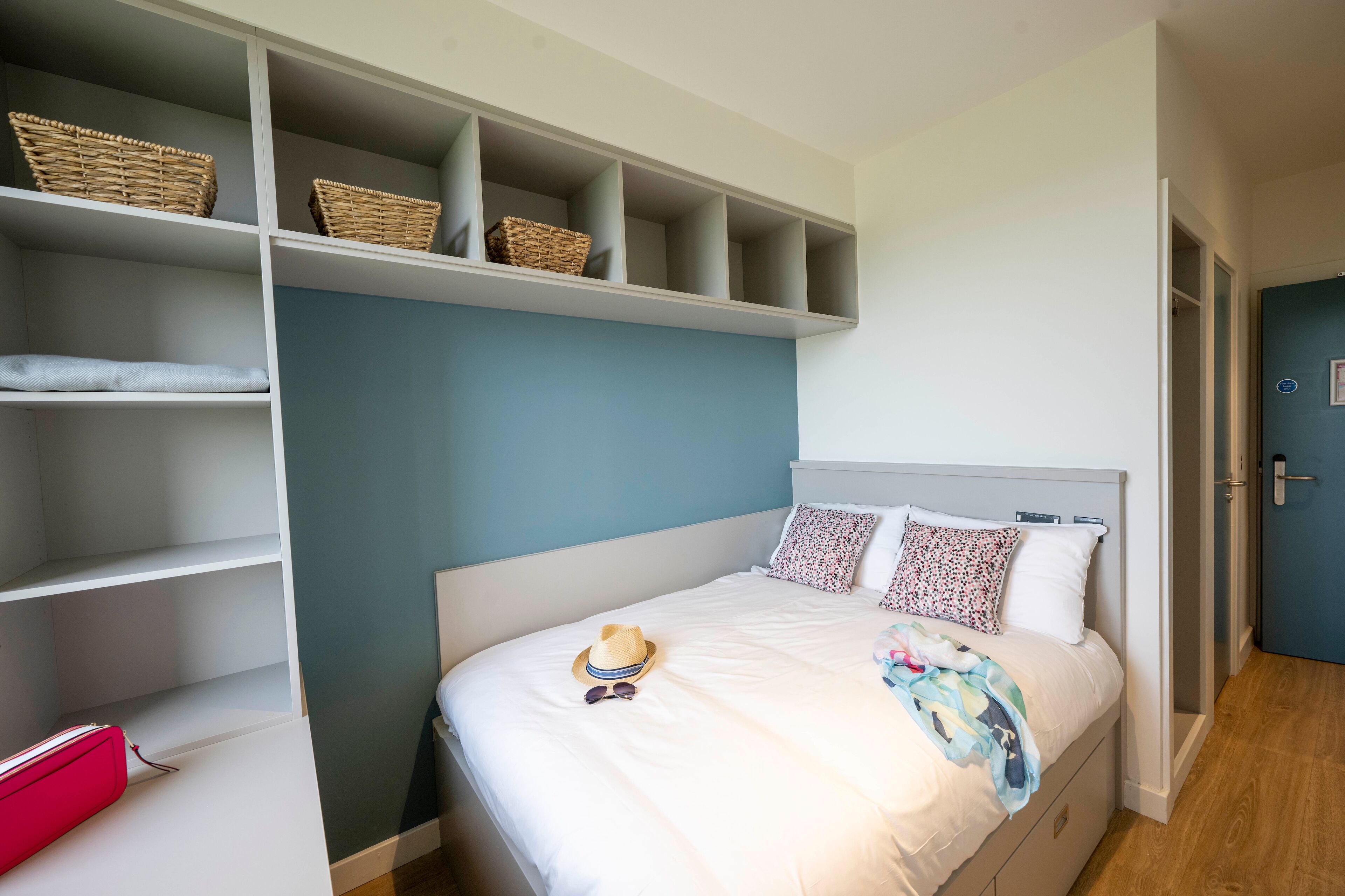 A bedroom with a bed, a wardrobe with shelves, and a door to another room.