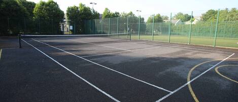 A tennis court with a net, surrounded by a green fence, and trees in the background.