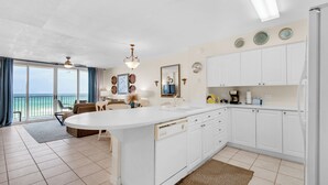A modern kitchen with a large island, white cabinets, and a view of the ocean.