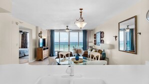 A spacious living area with a large window overlooking the sea, a dining table, and a modern kitchen area.